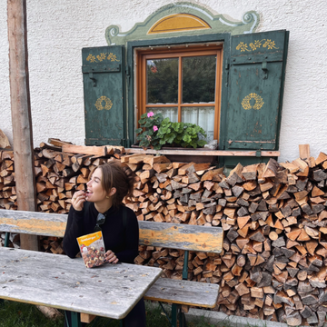Frau sitzt lachend auf einer Bank und isst eine Nuss aus der Seeberger Packung