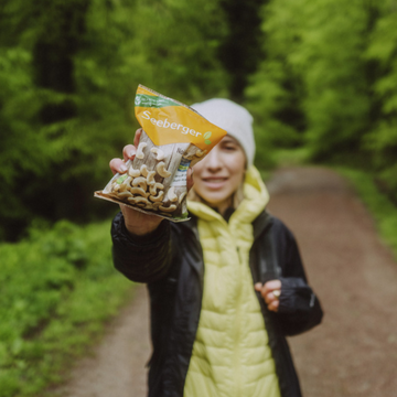 Frau im Wals hält eine Packung Cashewkerne in die Kamera