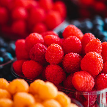 Himbeeren liegen in Schale, umgeben von verschiedenen Beeren in einem Marktstand.