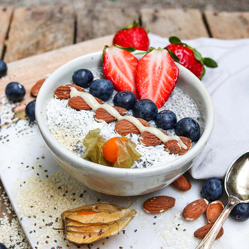 Schüssel mit Chia-Pudding, Mandeln, Beeren und Physalis auf Holztisch, dekoriert und servierfertig.