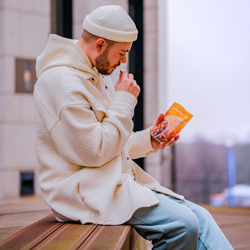 Ein Mann isst einen Snack, während er auf einer Bank draußen sitzt.
