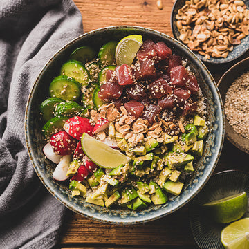 Schüssel enthält frischen Thunfisch, Avocado und Gemüse, garniert mit Sesam, auf Holztisch.